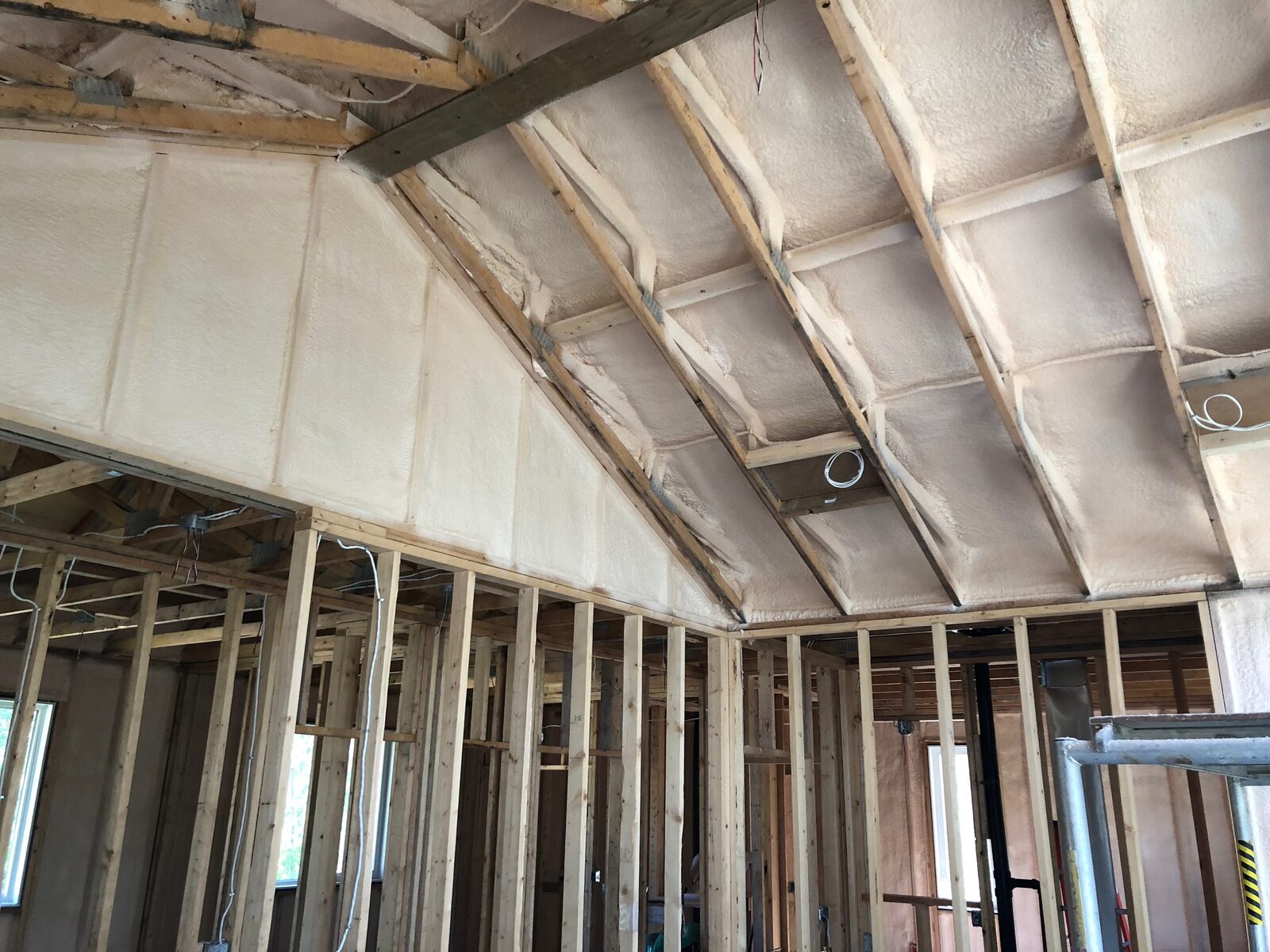 Vaulted ceiling and gable end wall sprayed with closed-cell foam above open interior partition framing