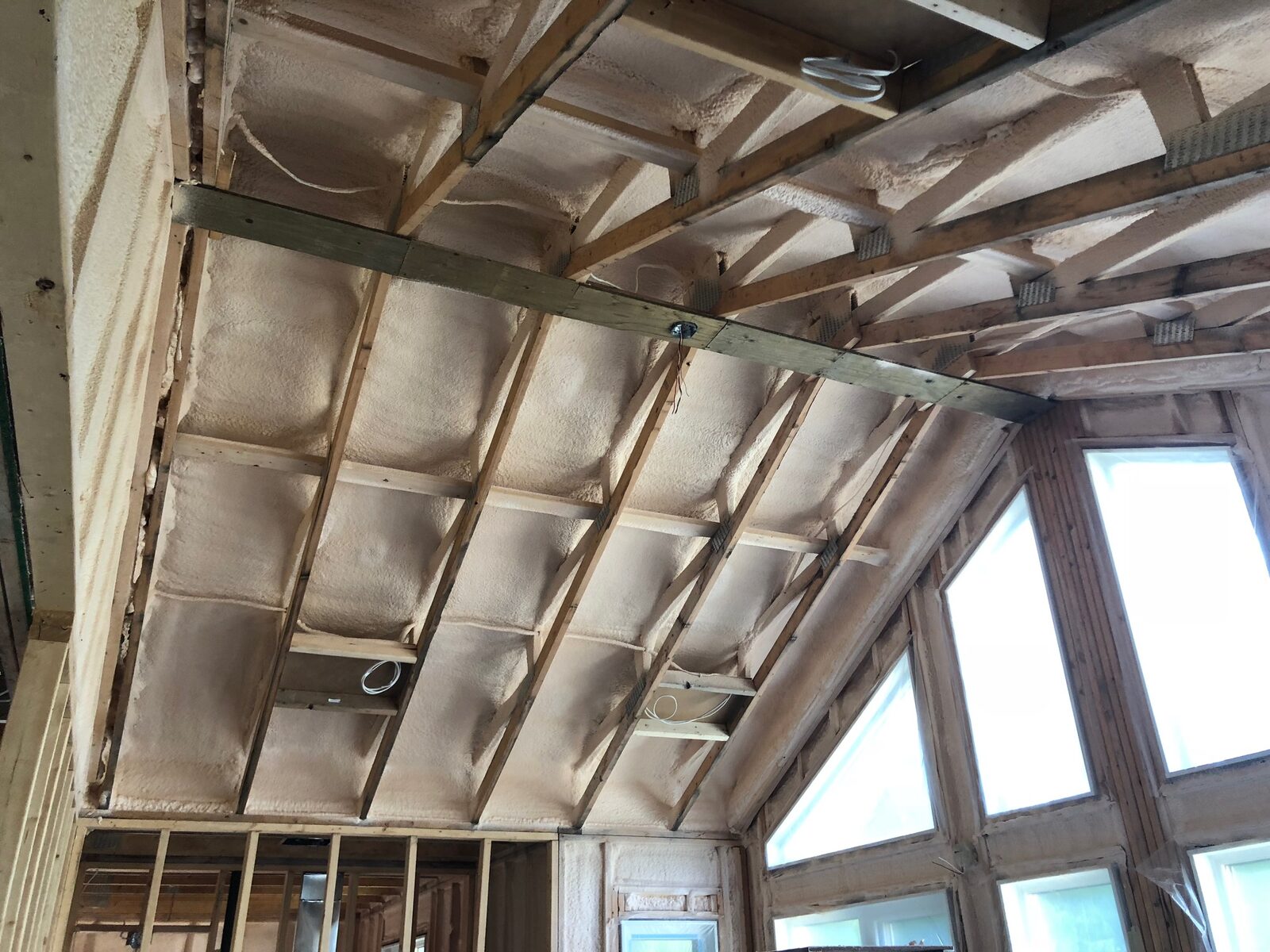 Looking up into a shallow vaulted ceiling with closed-cell spray foam filling each rafter bay and electrical boxes roughed in
