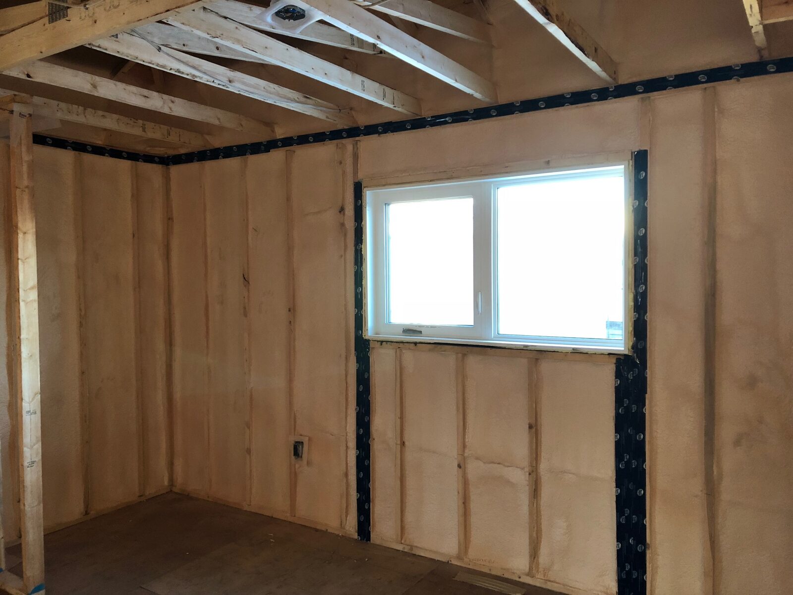 Bedroom wall with closed-cell spray foam and black tape running around the window rough opening and along the top plate